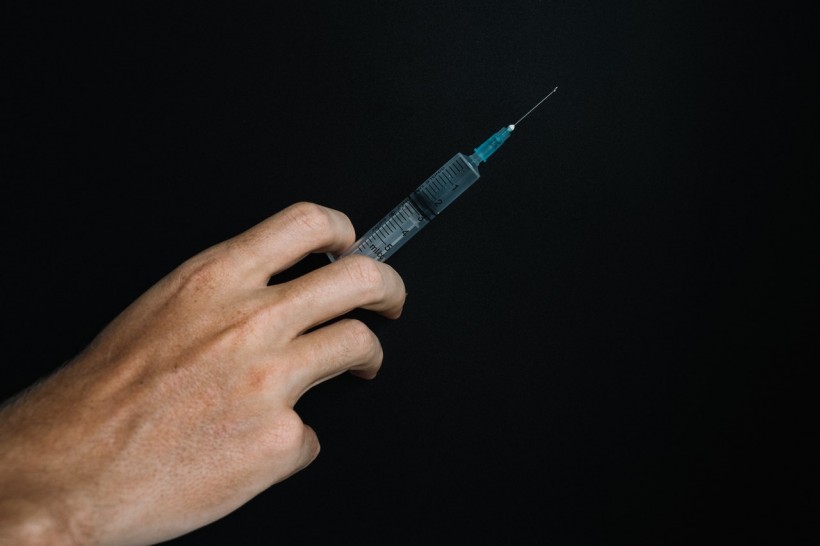 person-holding-a-syringe-on-black-background-5857415/