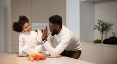 Black father with daughter near table with fruits in kitchen