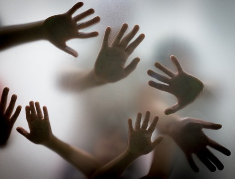 Many hands in silhouette pressed against frosted glass