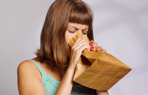 woman having a panic attack using paper bag to calm herself