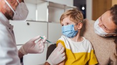 Boy looking at doctor holding vaccine injection in center - stock photo