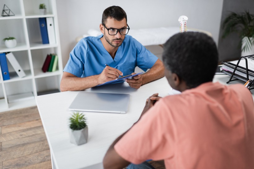 young doctor writing clipboard while listening mature african american patient