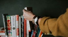 person picking white and red book on bookshelf