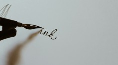 closeup photography of person holding black fountain pen writing ink text on white paper