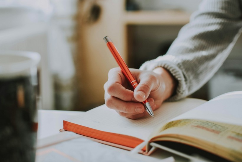 person holding on red pen while writing on a notebook