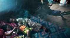 Yonta ,6, rests with her sister Montra,3, and brother Leakhena, 4months under a mosquito bed net keeping dry from the monsoon rain July 18, 2010 in Prey Mong kol village in Pailin province.
