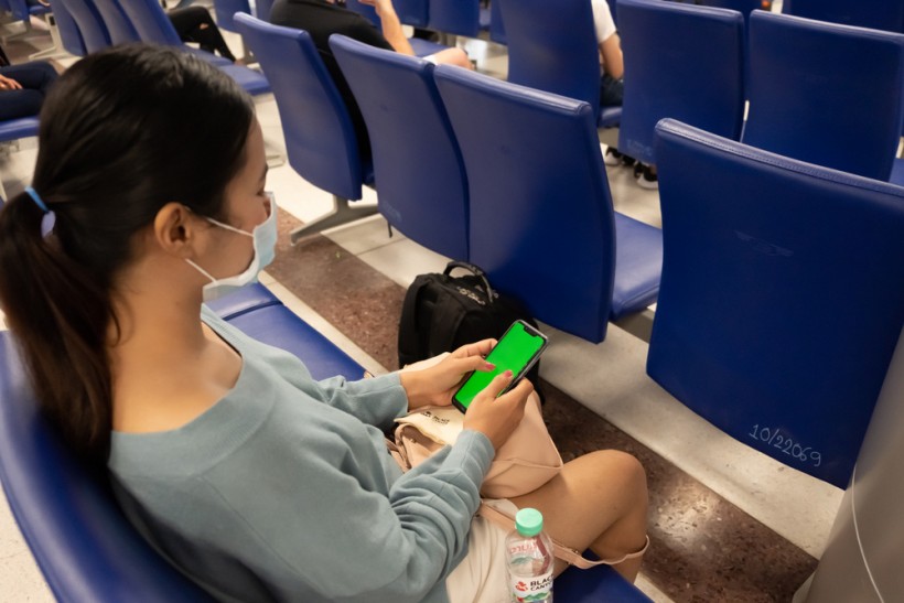 Thai lady texting on the phone at the airport. Asian girl use a protection mask for coronavirus or covid 19 in airport. - stock image
