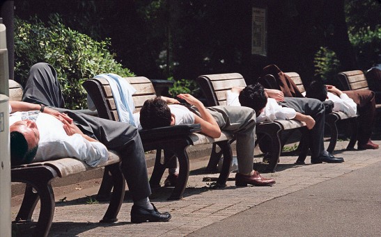 Japanese businessmen take naps on benches in Hibiya Park