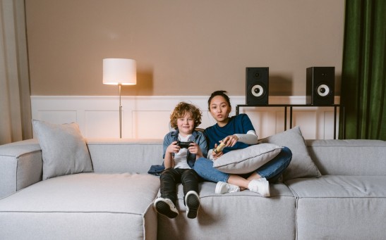 A Woman and a Kid Holding Video Game Controllers while Sitting on a Sofa