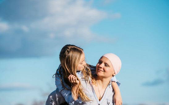 A woman with cancer is next to her daughter. A girl is hugging a woman happy