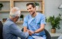 Happy general practitioner talking to senior man while shaking hands with him during a home visit